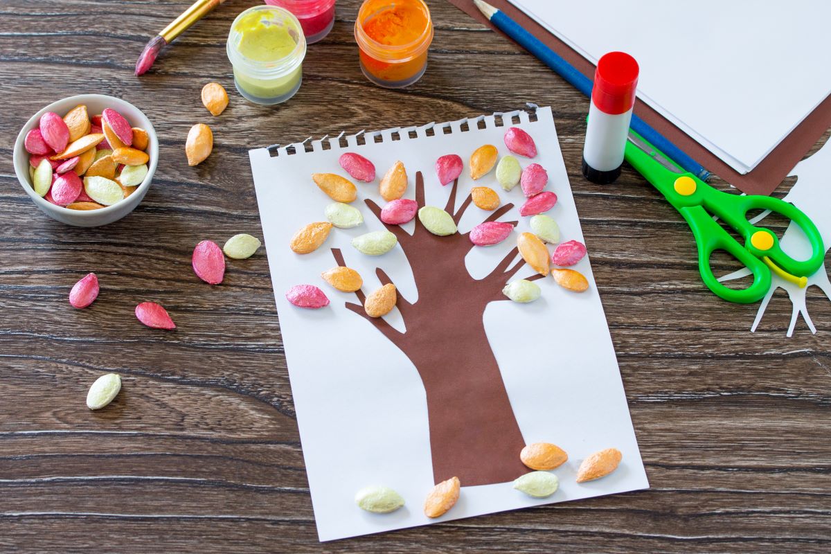 child's fall craft - brown tree with painted pumpkin seeds for leaves - in pink, orange, light green with scissors and glue stick